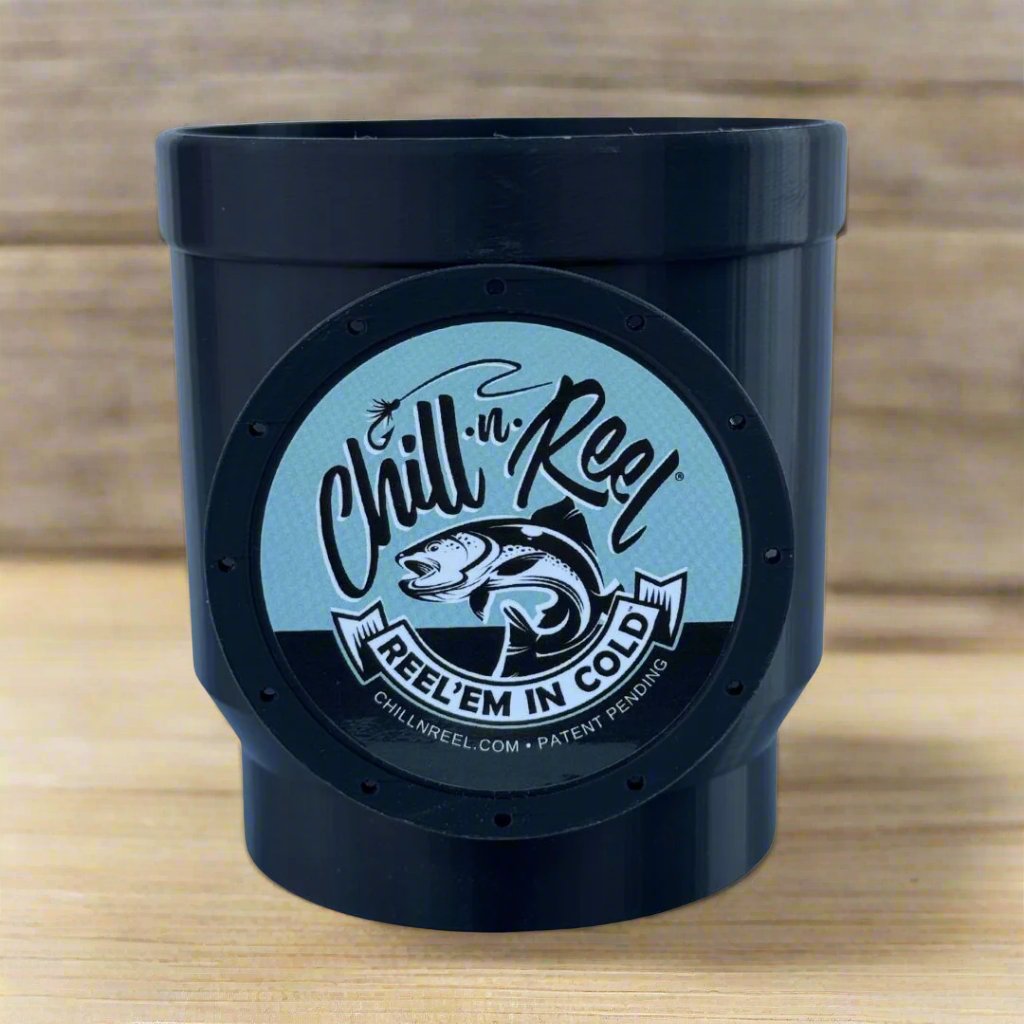A black, cylindrical drink holder from Chill-N-Reel® features a circular logo with a fish and the text "Reel 'Em In Cold," positioned on a wooden surface. This limited prototype includes the innovative Chill-N-Reel Tumbler Handle, ideal for fishing game enthusiasts.