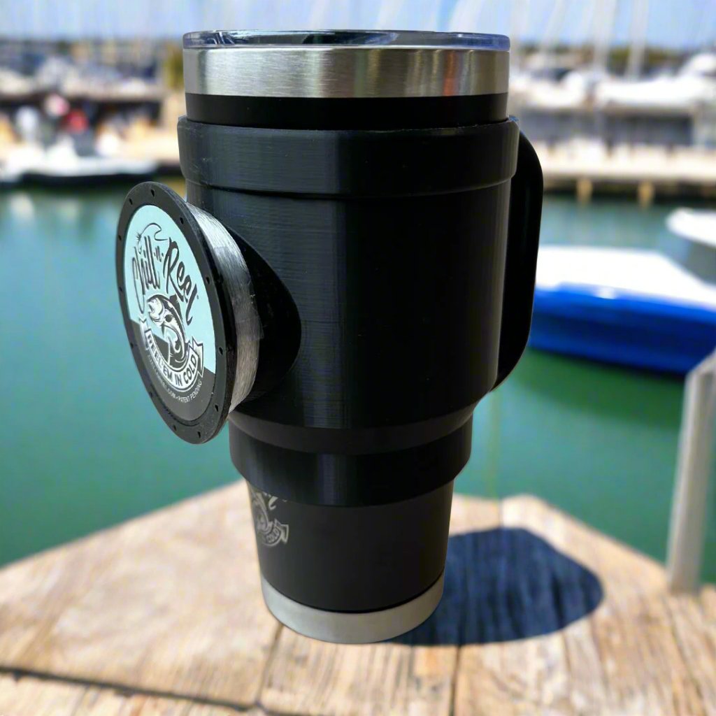 A 30oz Tumbler with a Chill-N-Reel® Tumbler Handle (Prototype) is perched on a dock overlooking a marina. Several boats and blurred water are visible in the background under a bright blue sky, making it the perfect fishing and drinking accessory.