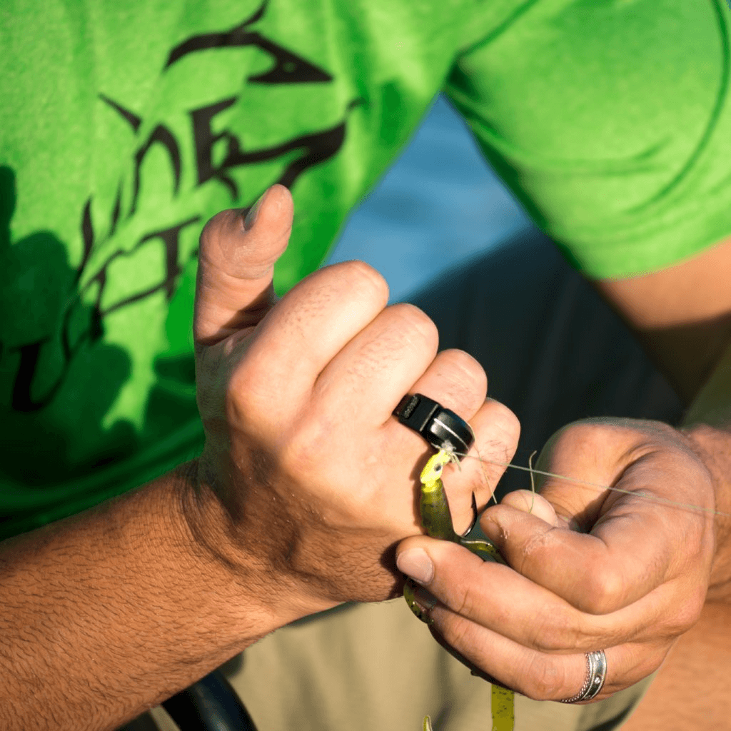 A person in a green shirt and ring prepares tackle outdoors, using the Line Cutterz "TRIPLE PLAY" Fishing Line Cutter Multi-Pack to cut fishing line and soft plastic lures.