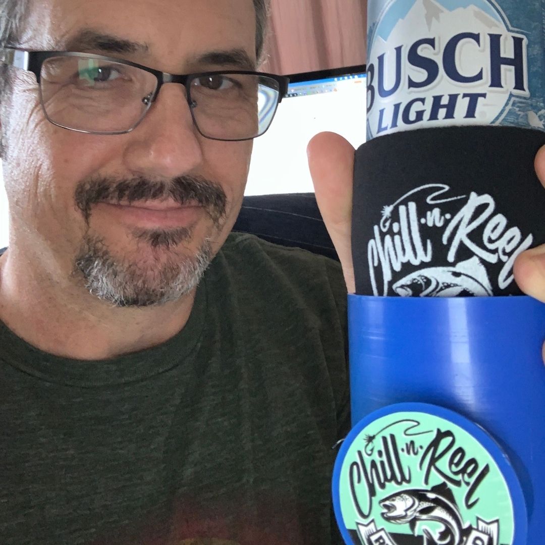 A man with glasses and a short beard holds a Busch Light can wrapped in a Chill-N-Reel koozie. He is wearing a green t-shirt and smiling slightly.