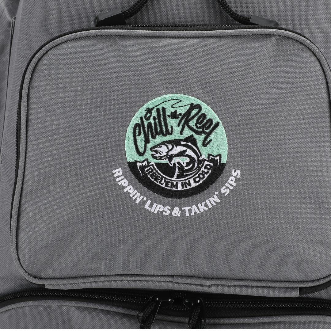 This Chill-N-Reel® Fishing Tackle Backpack with Cooler Top features a stylish light green circular patch embroidered with a fish and the phrases "Chill N' Reel," "Reel 'Em in Cold," and "Rippin' Lips & Takin' Sips." Its gray design makes it perfect for practical yet fashionable tackle storage.