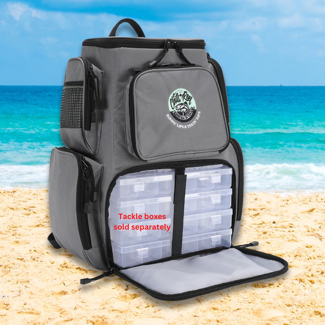 A gray Fishing Tackle Backpack with Cooler Top by Chill-N-Reel® rests open on a sandy beach, revealing clear tackle boxes labeled "Tackle boxes sold separately." The backdrop showcases a vibrant blue ocean and sky, ideal for a day of fishing.