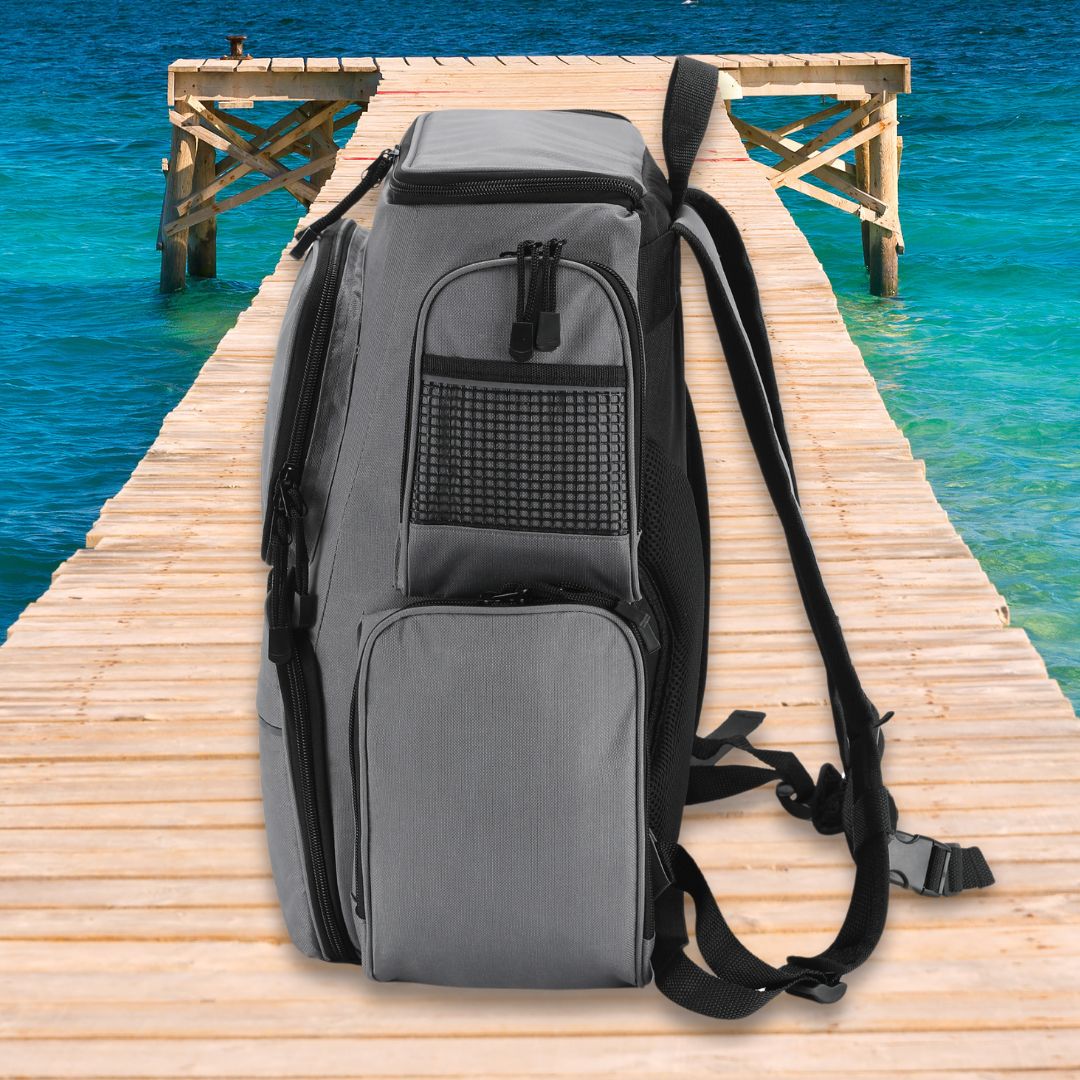 A Chill-N-Reel® Fishing Tackle Backpack with Cooler Top sits upright on a wooden dock overlooking a calm, turquoise ocean. The backpack, by Chill-N-Reel®, features multiple compartments and mesh pockets ideal for storing tackle. Its cooler top is perfect for keeping your refreshments chilled as the dock stretches into the horizon.