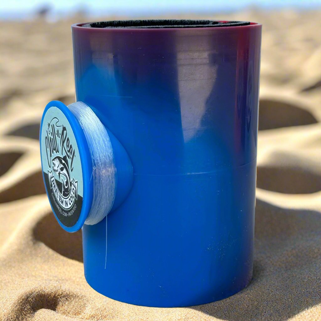 A Mystery Color Chill-N-Reel from Chill-N-Reel®, featuring a round side attachment with the "Oahu Reel" logo and a fish image, is partially buried in beach sand. Fishing line peeks out from the attachment, suggesting it as a Limited Edition option for fishing enthusiasts.