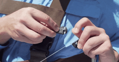 Close-up of hands in a blue shirt attaching a fishing reel to a rod while wearing the Line Cutterz "TRIPLE PLAY" Fishing Line Cutter Multi-Pack ring, carefully prepping gear outdoors.