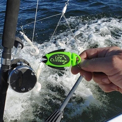 A hand holds the Line Cutterz Dual Hybrid Micro Scissors by Line Cutterz near a fishing rod and reel on a boat, with choppy water in the background.