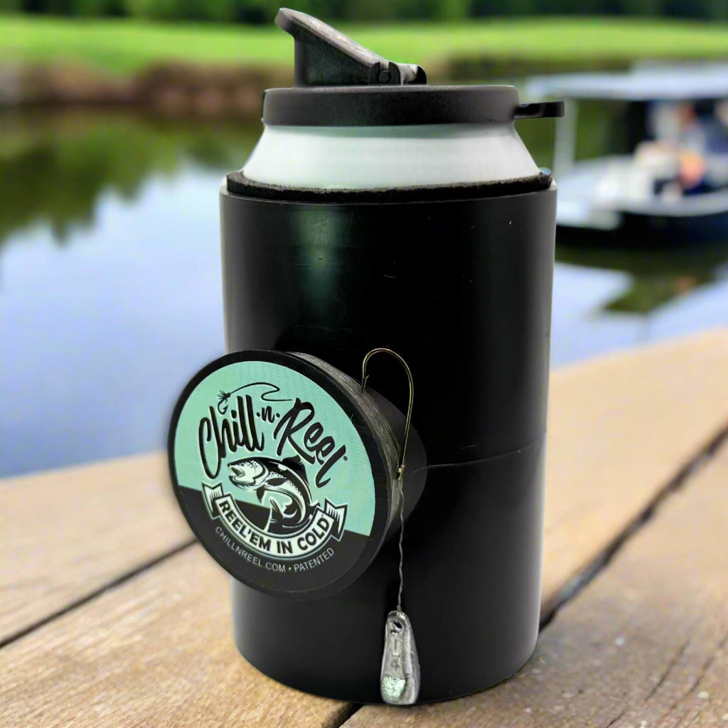 The Original Chill-N-Reel by Chill-N-Reel, a black can cooler with a fishing reel, rests on wood by a lake—blurred boats and trees behind—making it the perfect fun fishing gift.
