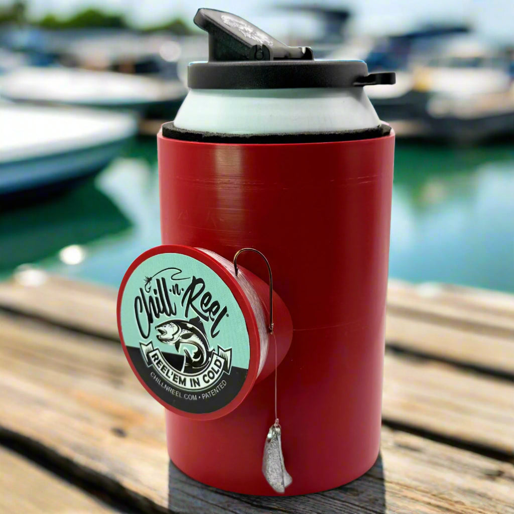 The Original Chill-N-Reel by Chill-N-Reel is a red can cooler with a built-in hand-line fishing reel, shown on wood near water and blurred boats—a unique gift idea for any angler.