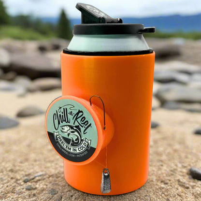The Original Chill-N-Reel by Chill-N-Reel is a bright orange can cooler with a black lid and a mounted hand-line fishing reel, shown on sandy ground with rocks and greenery in the background. Makes a fun fishing gift!.