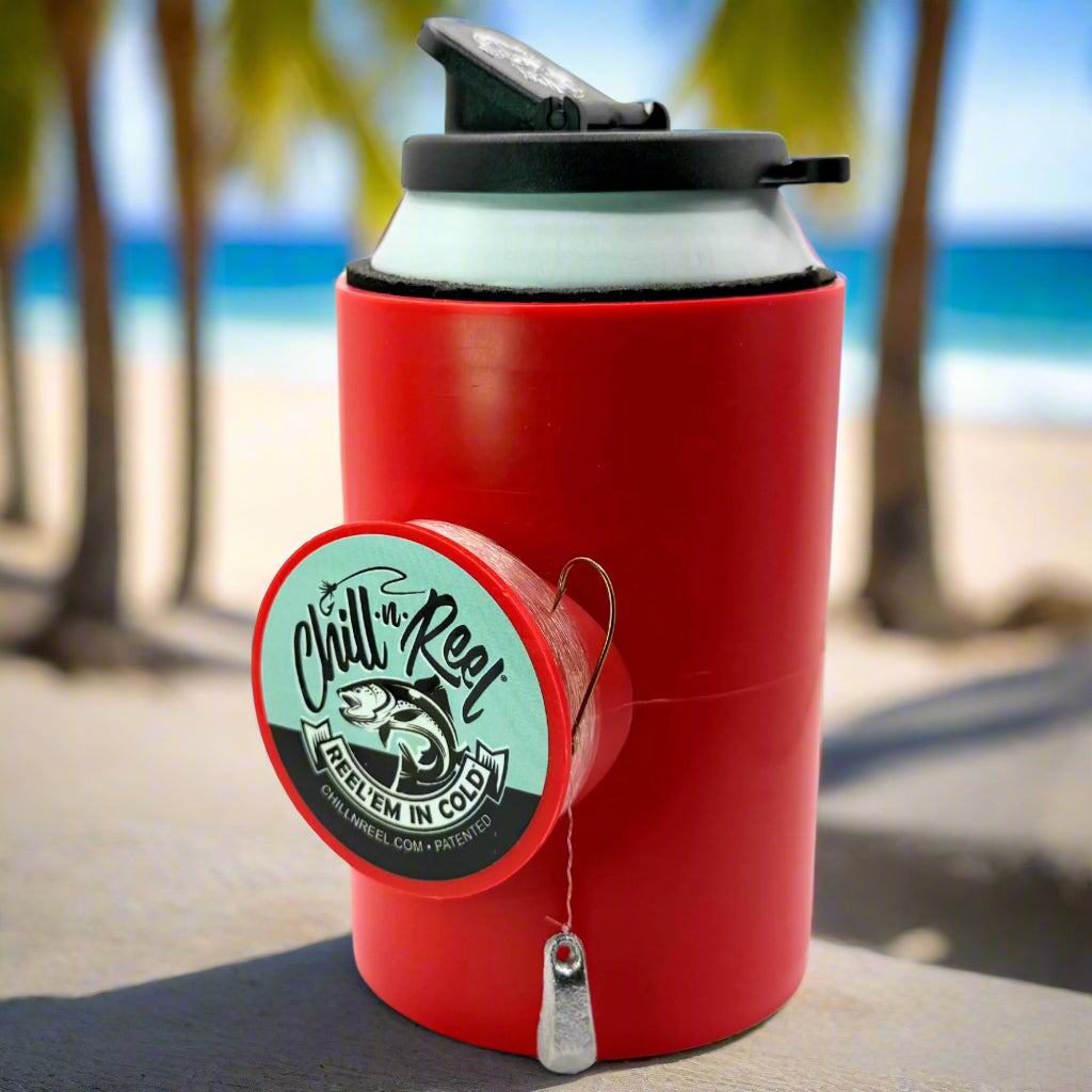 A red Original Chill-N-Reel can cooler by Chill-N-Reel, featuring a built-in hand-line fishing reel, sits on a beachside table with palm trees and the ocean blurred in the background.