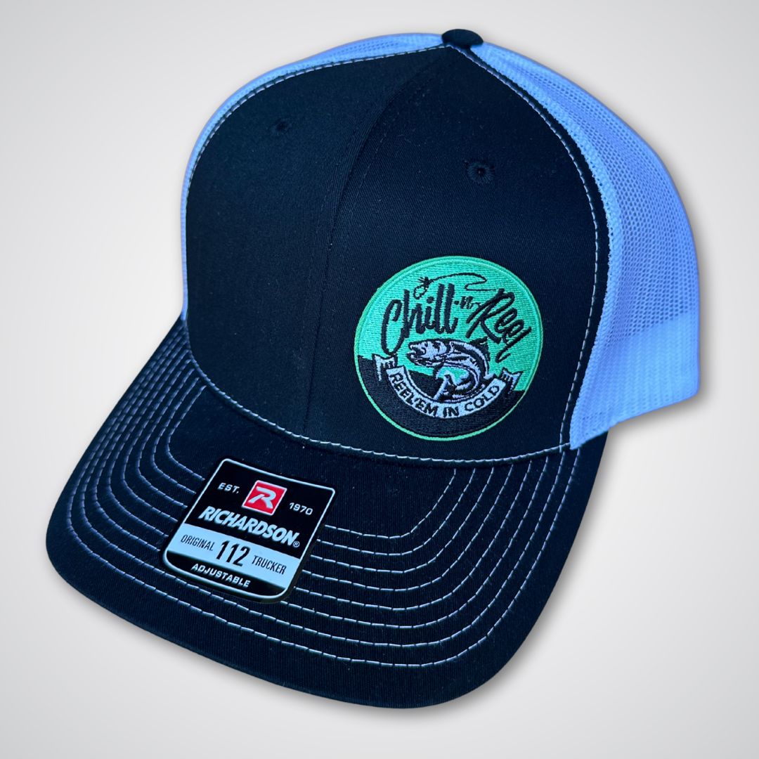 The Chill-N-Reel Trucker Hat is a black and white cap with a curved bill, "Reel 'Em In Cold" fish patch, and Richardson 112 sticker. Perfect for fishing fans, it's a must-have from Chill-N-Reel.