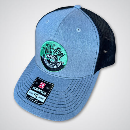 The Chill-N-Reel Trucker Hat features a blue and black design with a mesh back, a green and black fishing patch with fish graphic on the front, and a Richardson 112 sticker label on the brim.