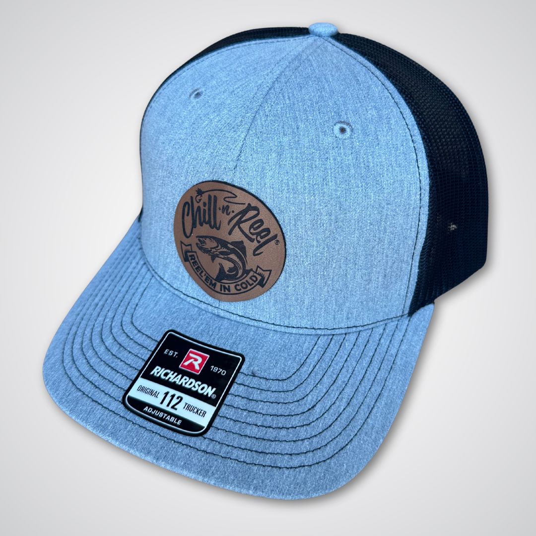 The Chill-N-Reel Trucker Hat by Chill-N-Reel features light gray and black panels, a brown circular front patch with a fish graphic, and a "Richardson 112 Trucker" sticker on the brim.
